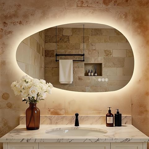 Miroir asymétrique sans cadre, rétroéclairé et fixé au mur dans une salle de bain claire.